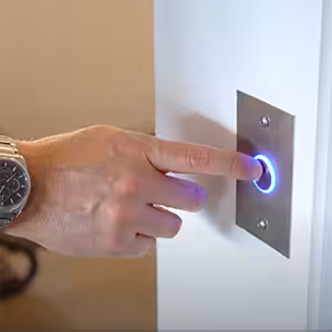 Hand pressing illuminated doorbell button in a compass lift.