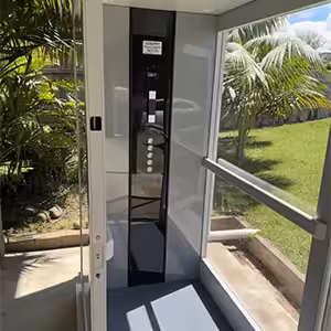 Modern glass iconic lift in residential garden setting.