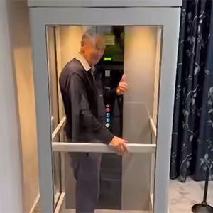 Elderly man inside an iconic home lift giving thumbs up.