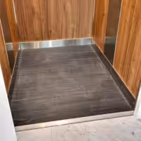 Modern lift interior with wooden panels and tiled floor.