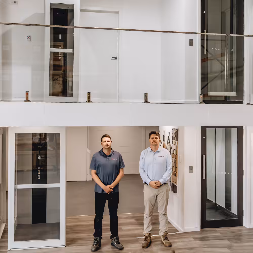 Two men standing in modern glass balcony showing home lifts to clients.